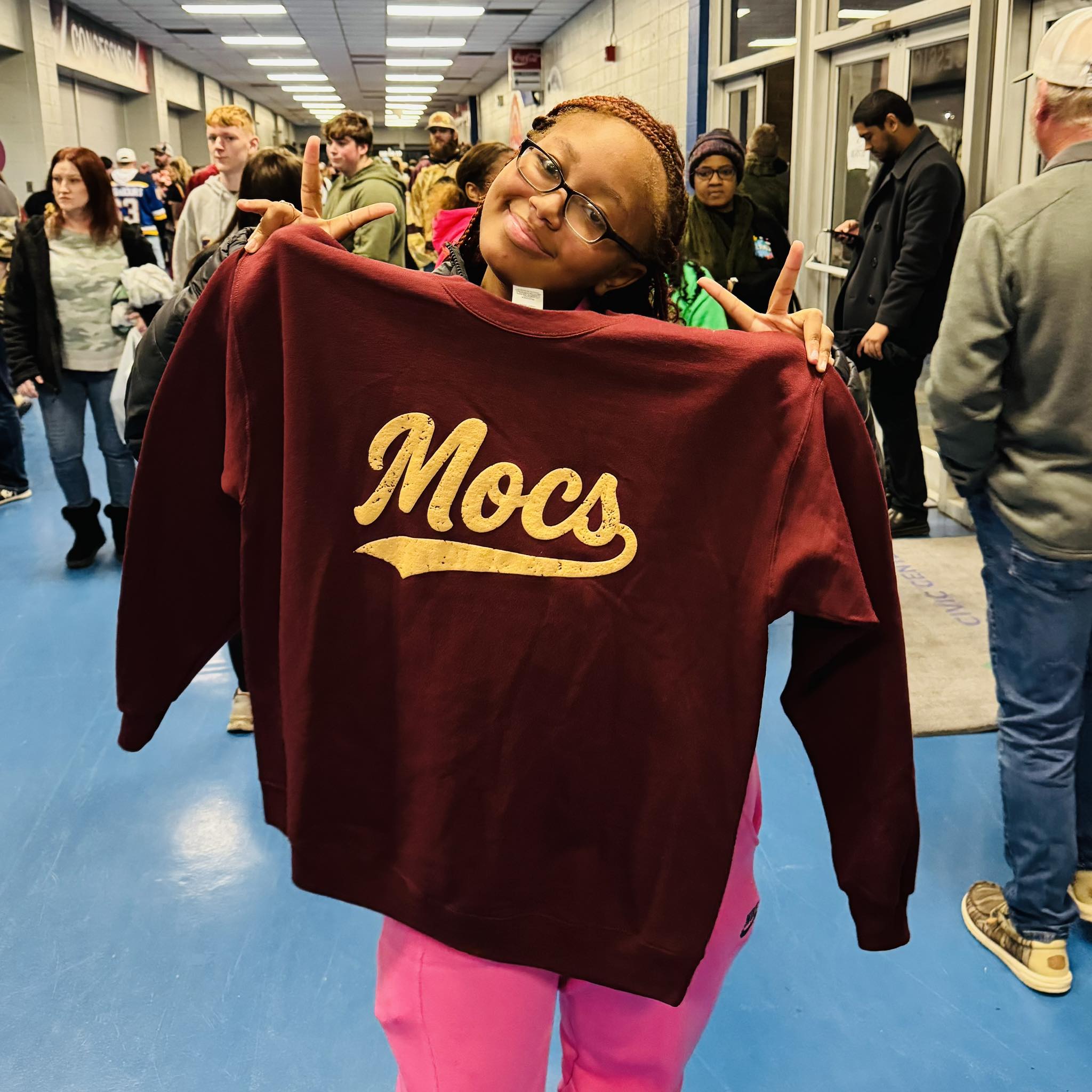 A girl holding a sweatshirt that says Mocs.